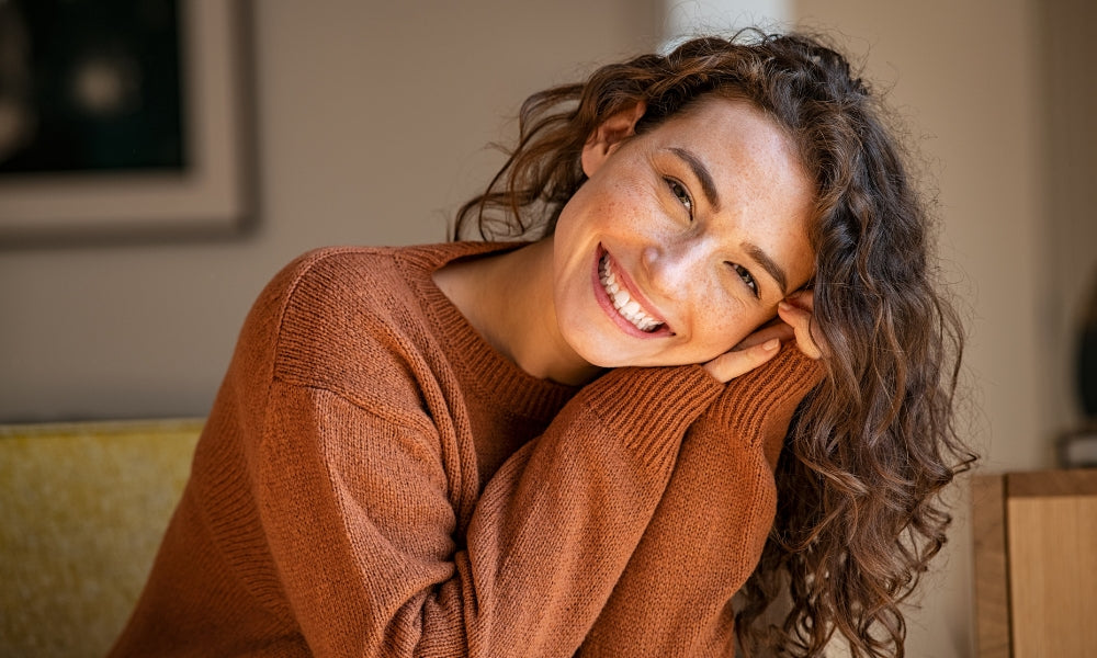 woman is smiling and holding her head on a side in beige looking home
